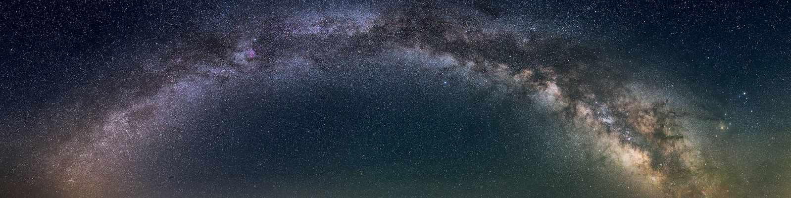 Panoramic view of the Milky Way arching across the night sky with golden star clouds, pink and purple nebulae, and a faint green glow near the horizon. Image courtesy of the National Parks Conservation Association.